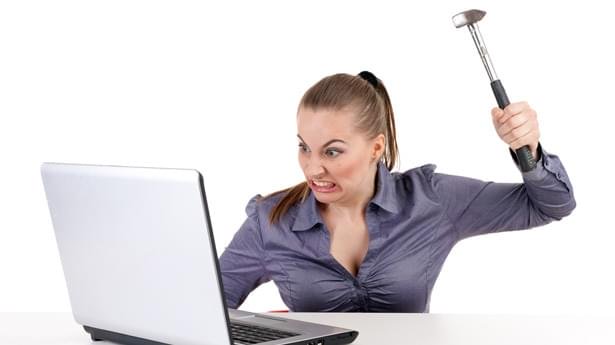 A woman with a hammer in her hand ready to strike her laptop