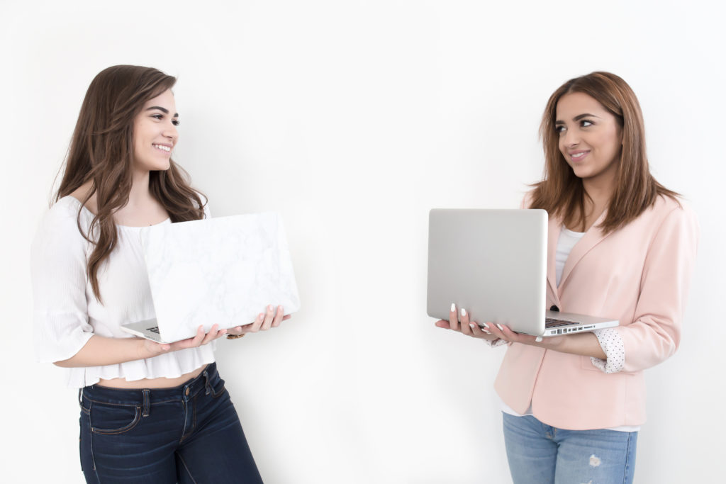 Two ladies holding laptops and staring at each other